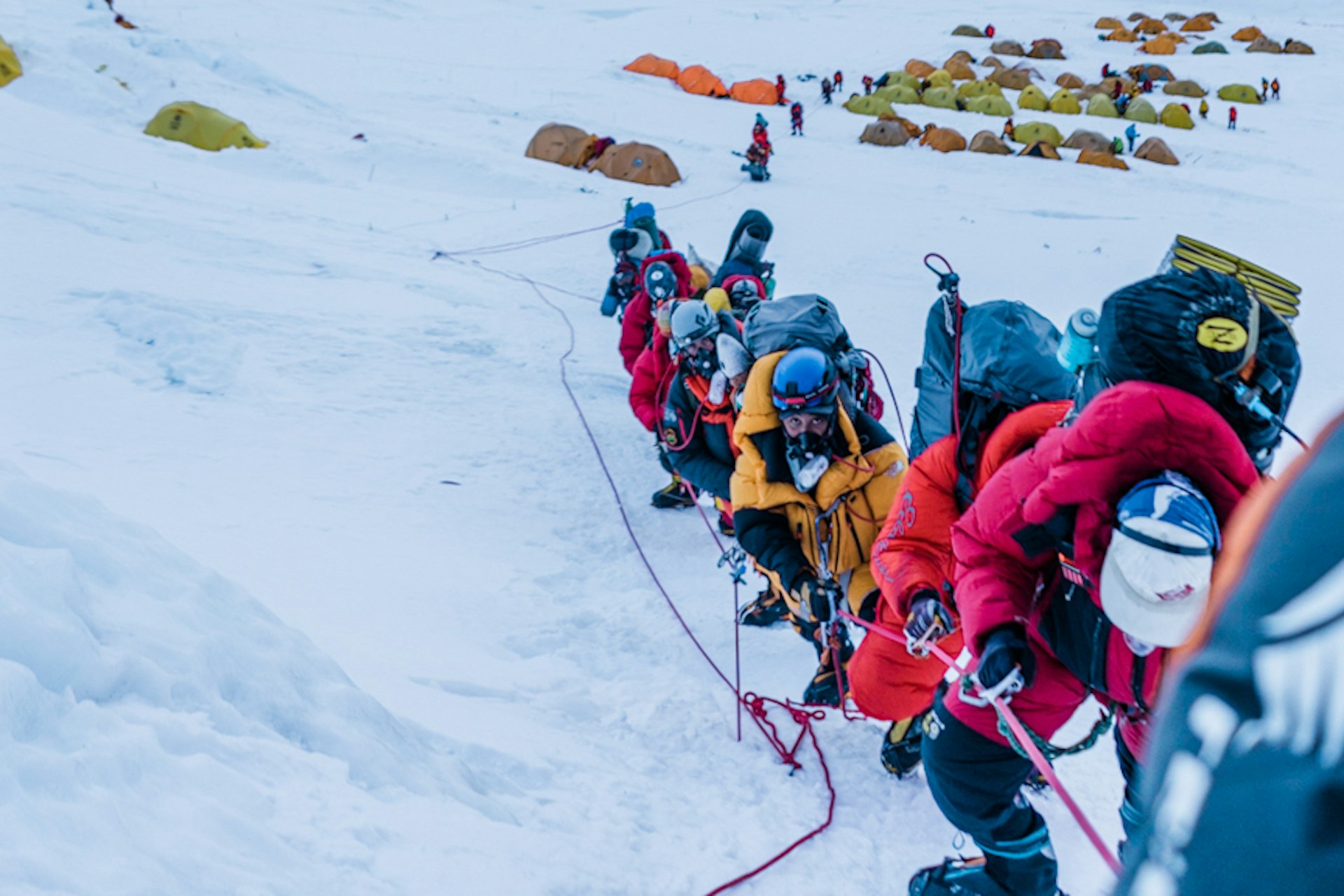 Members of the Full Circle Everest team in a line of climbers making their way up the mountain, with one of the camps in the background