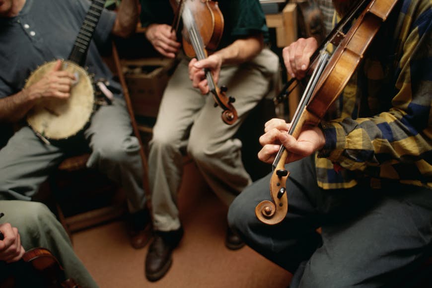 Three musicians play a banjo and two violins in a bluegrass style