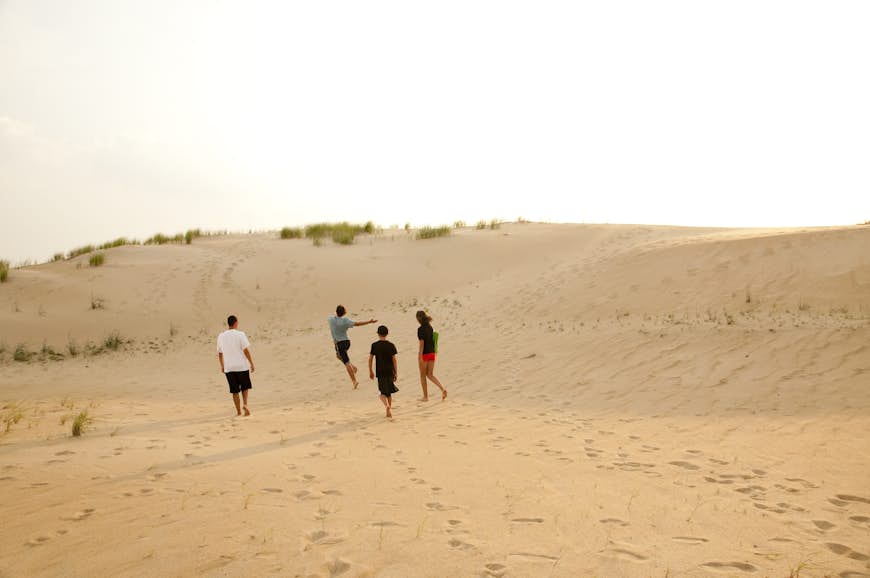 Four teenagers run towards a sand dune during sunset at Jockey's Ridge
