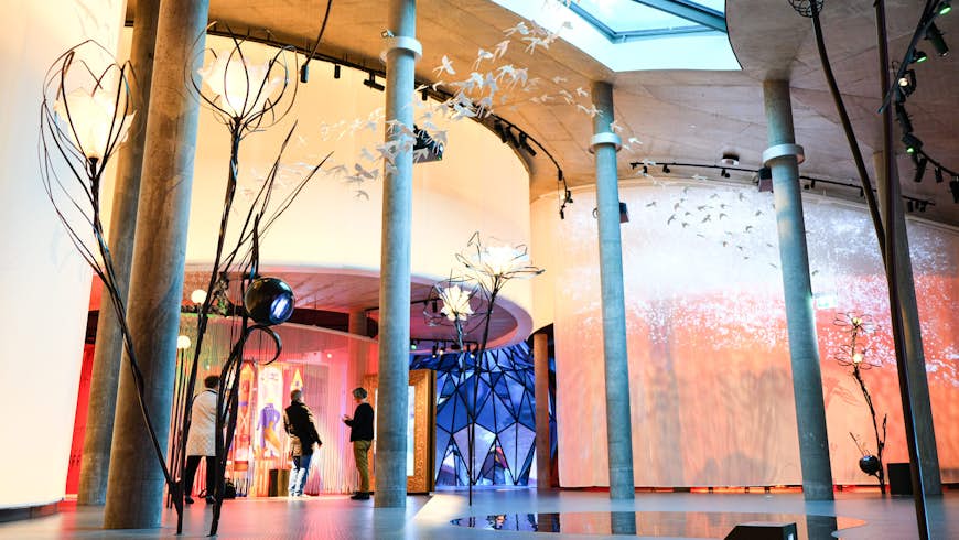 A large colourful curved wall with displays of light, with sculptures of giant flowers and bids soaring above