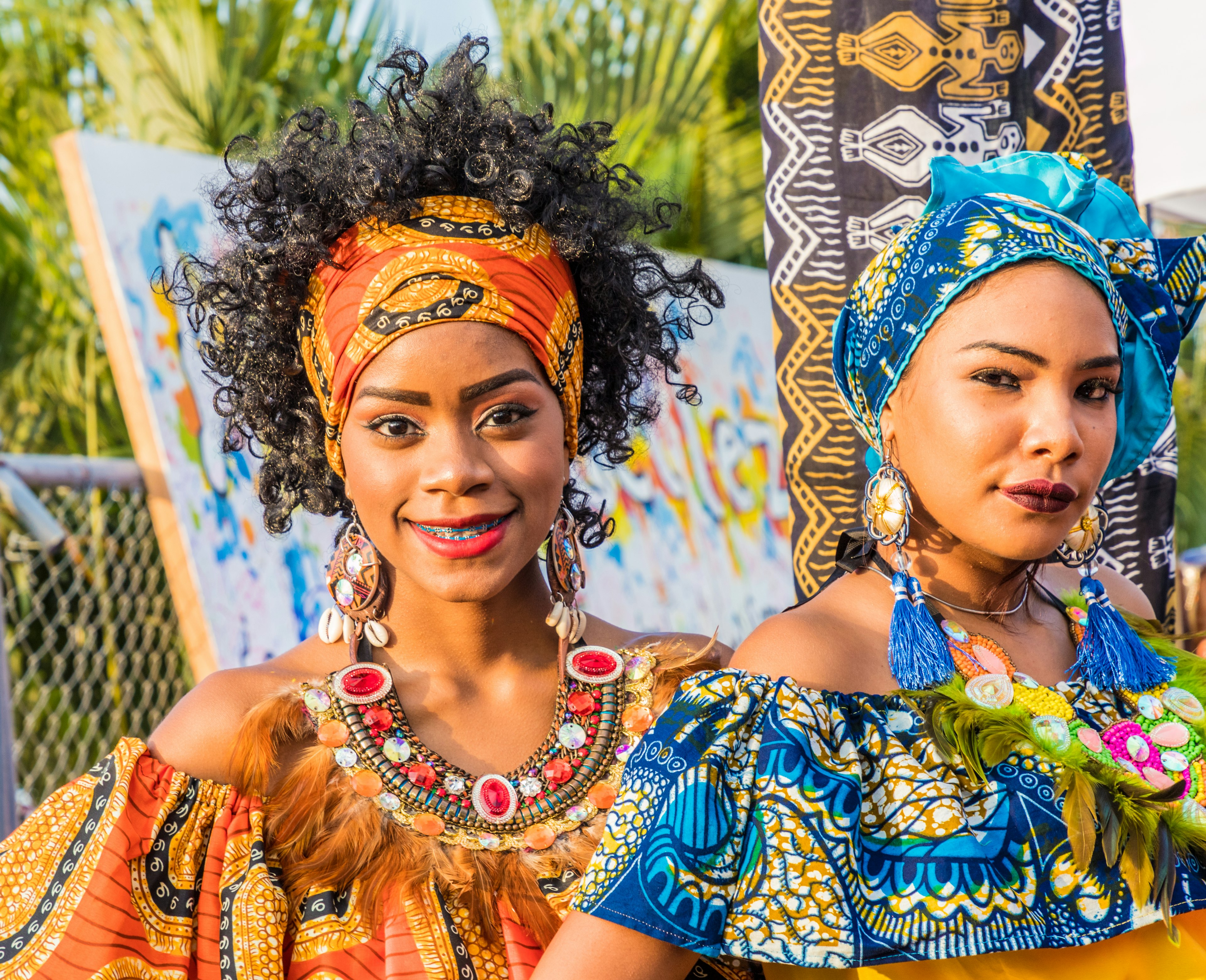 Two wearing colorful tradition garb and head scarves smile at the camera. 