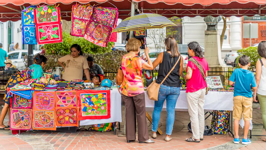 A group of travelers look over tables filled with souvenirs at an outdoor market in Panama City, Panama.