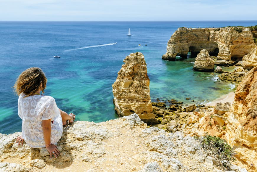 En kvinna sitter på klipporna och ser mot Praia da Marinha och dramatiska klippformationer, Algarve, Portugal