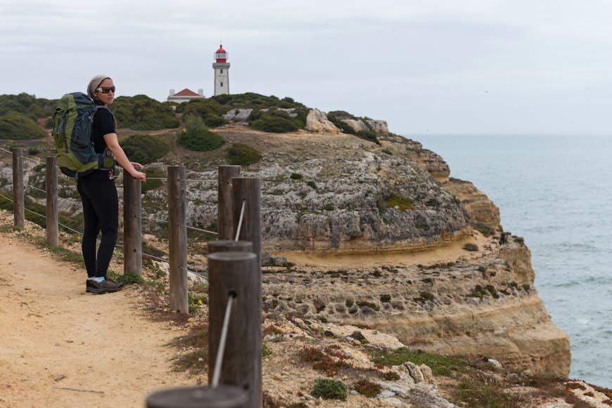 Une randonneuse sur le chemin des sept vallées suspendues (Percurso dos Sete Vales Suspensos) admire la vue sur le phare et les formations de schiste, Algarve, Portugal