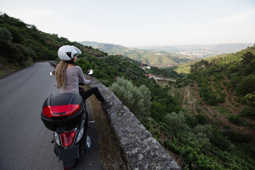 Female motorcyclist looks out onto a valley view on a serpentine road in the Douro Valley, Porto, Portugal