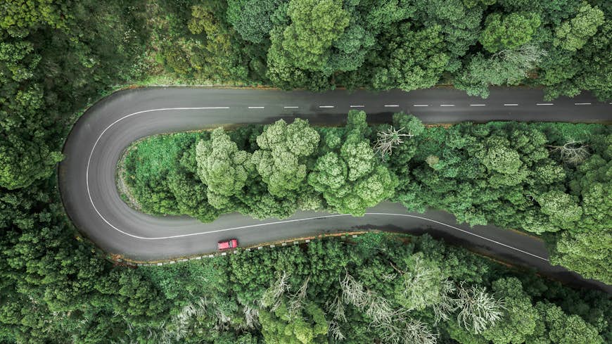 An aerial view of car driving on heavily curved road through a wooded mountain in Encumeada, Ribeira Brava, Madeira, Portugal