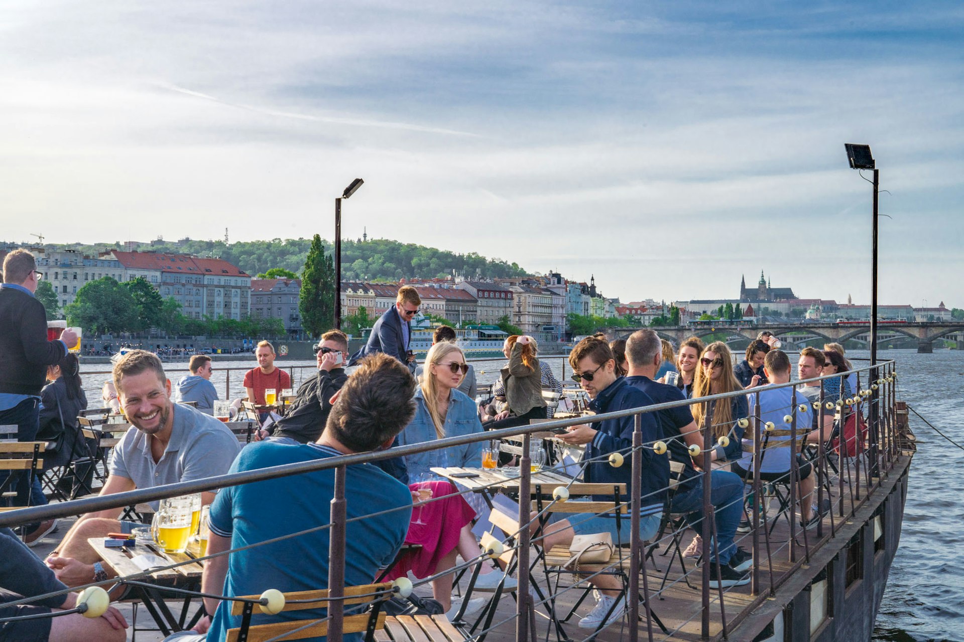 People sit on the deck of a boat on a river enjoying drinks on a sunny day