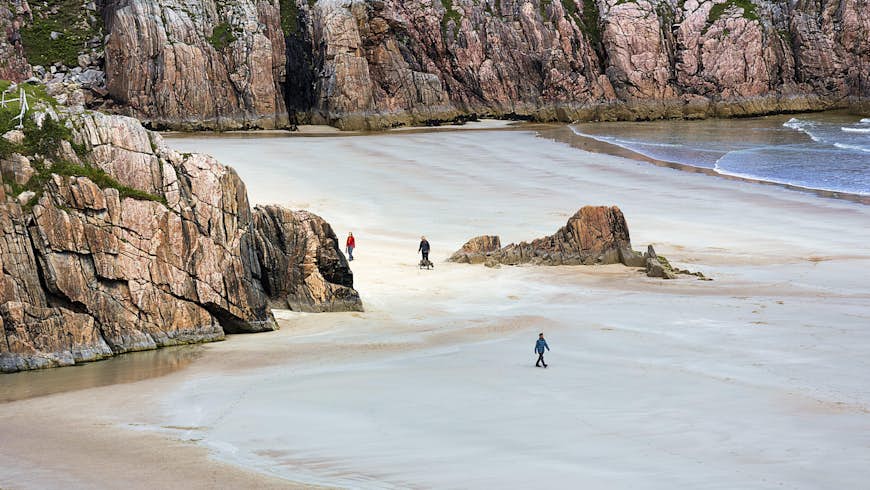 Walkers in a sandy bay with huge rocks towering over them, Rispond Bay, Durness, Scotland