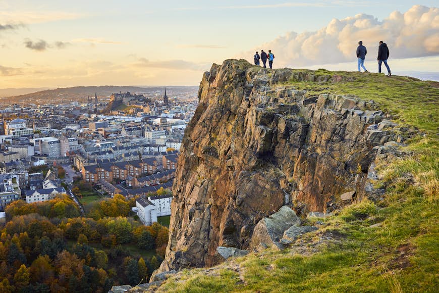 Group of people walking along cliff edge looking over Edinburgh 
