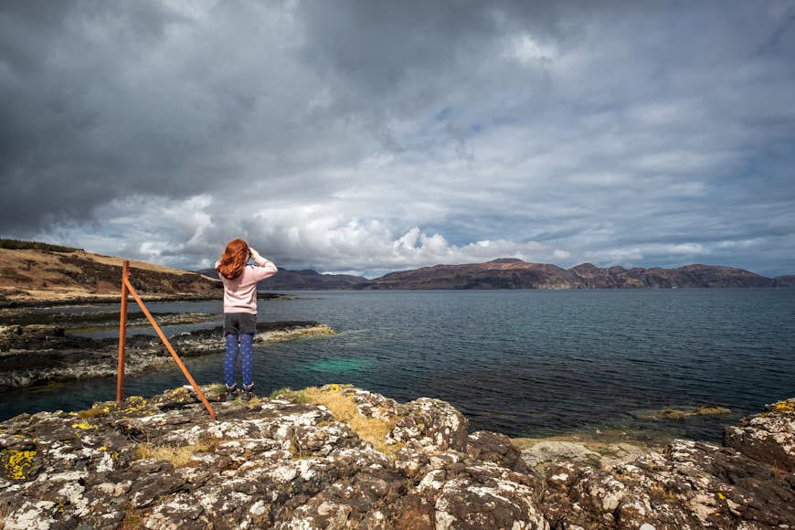 A young child stands looking out towards the water for wildlife in Scotland