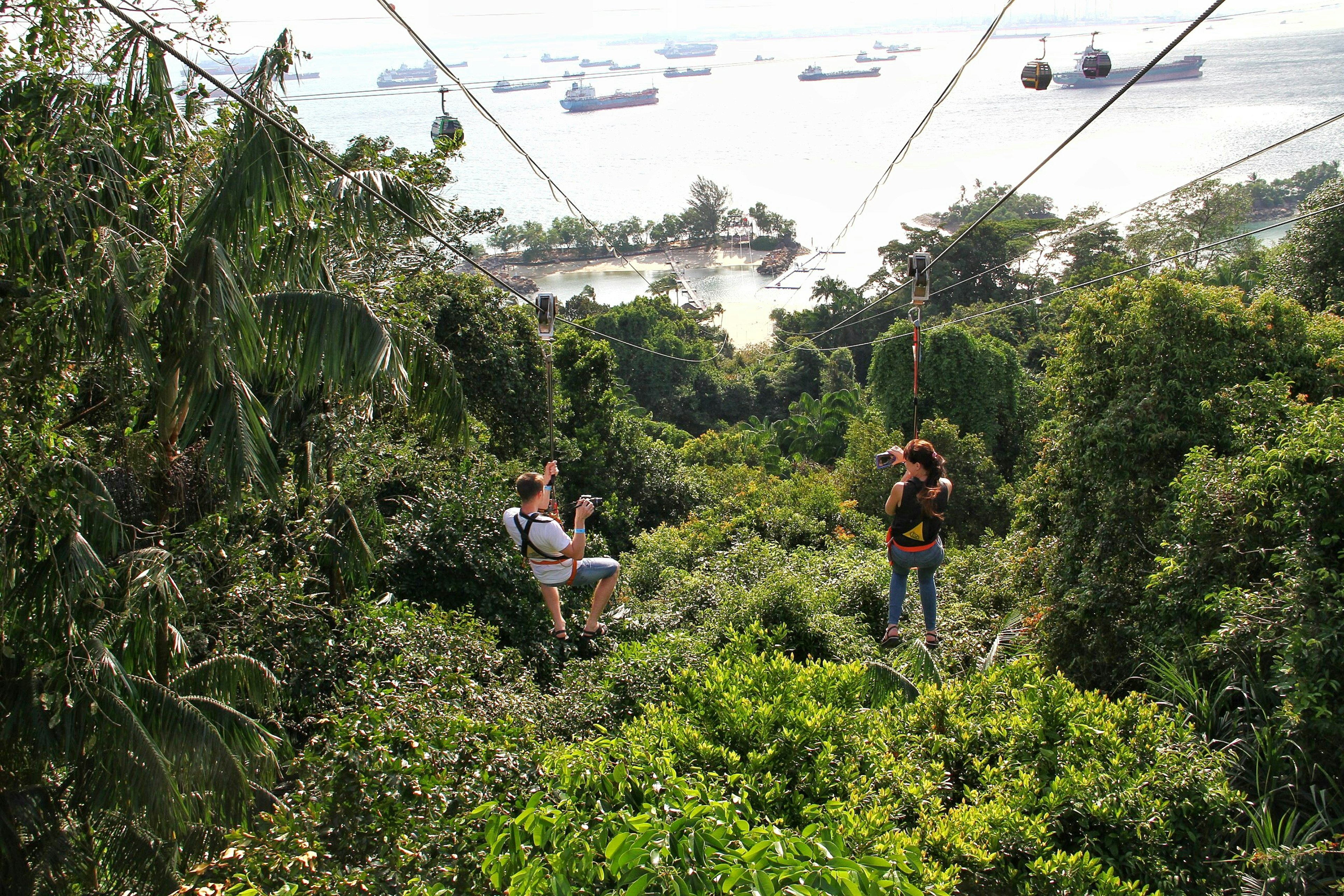 A couple flies down the MegaZip line to Siloso Beach, Sentosa Island, Singapore