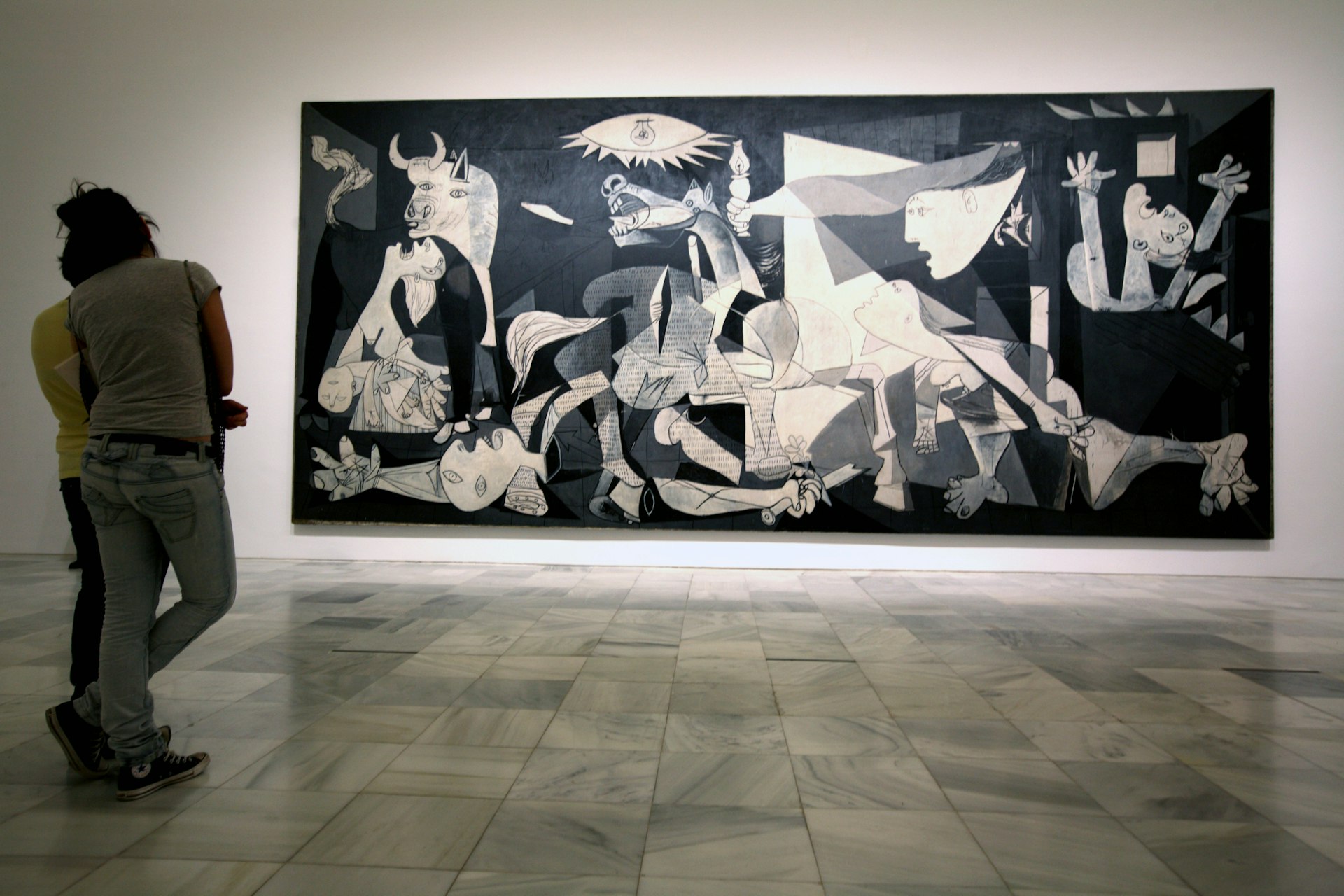 Two museum visitors look at Pablo Picasso's Guernica, a huge black-and-white abstract painting, in Reina Sofia National Art Museum, Madrid