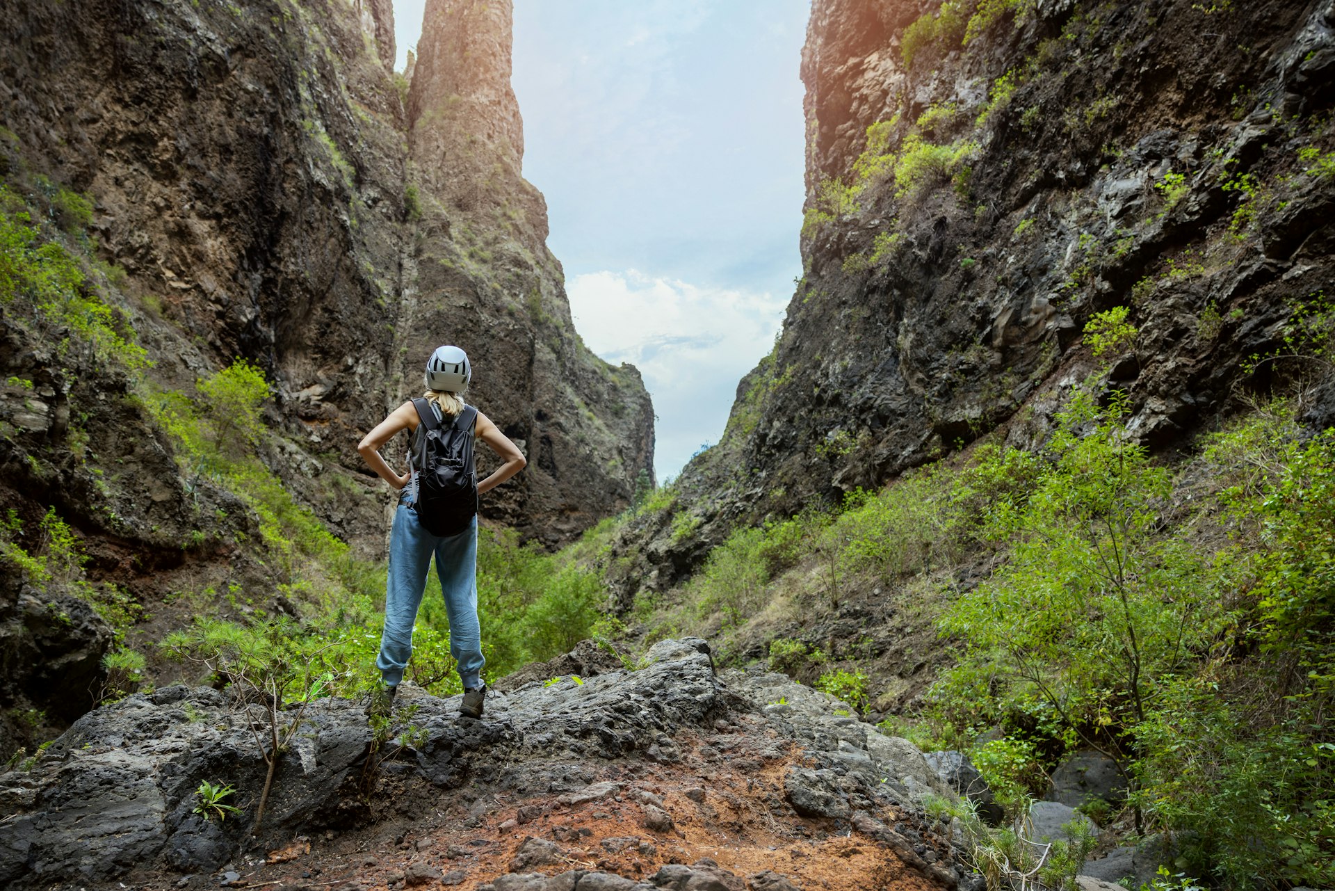 A woman wearing a helmet stands on a trail in the Barranco del Infierno, a sheer-sided rocky canyon in Tenerife. Canary Islands