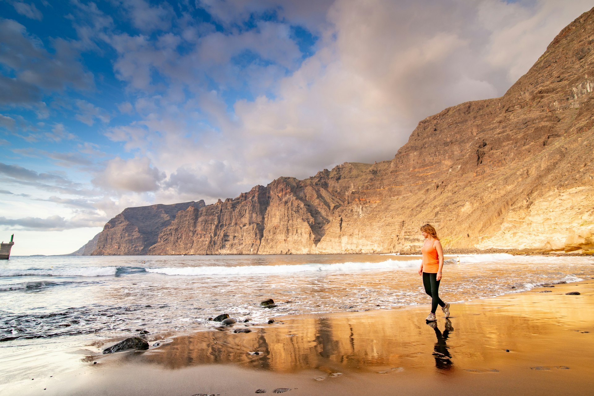 Adult woman walking along the beach in Tenerife, backed by huge sheer rocky cliffs
