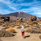 A person in a white hat and red plants walks through shrubs along a mountain trail in the Teide National Park in Tenerife, Canary Islands, Spain. Europe.
