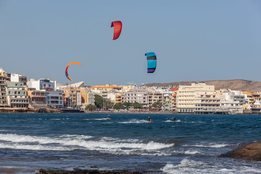 Three kitesurfing kites fly above surf at the beachside village of El Medano