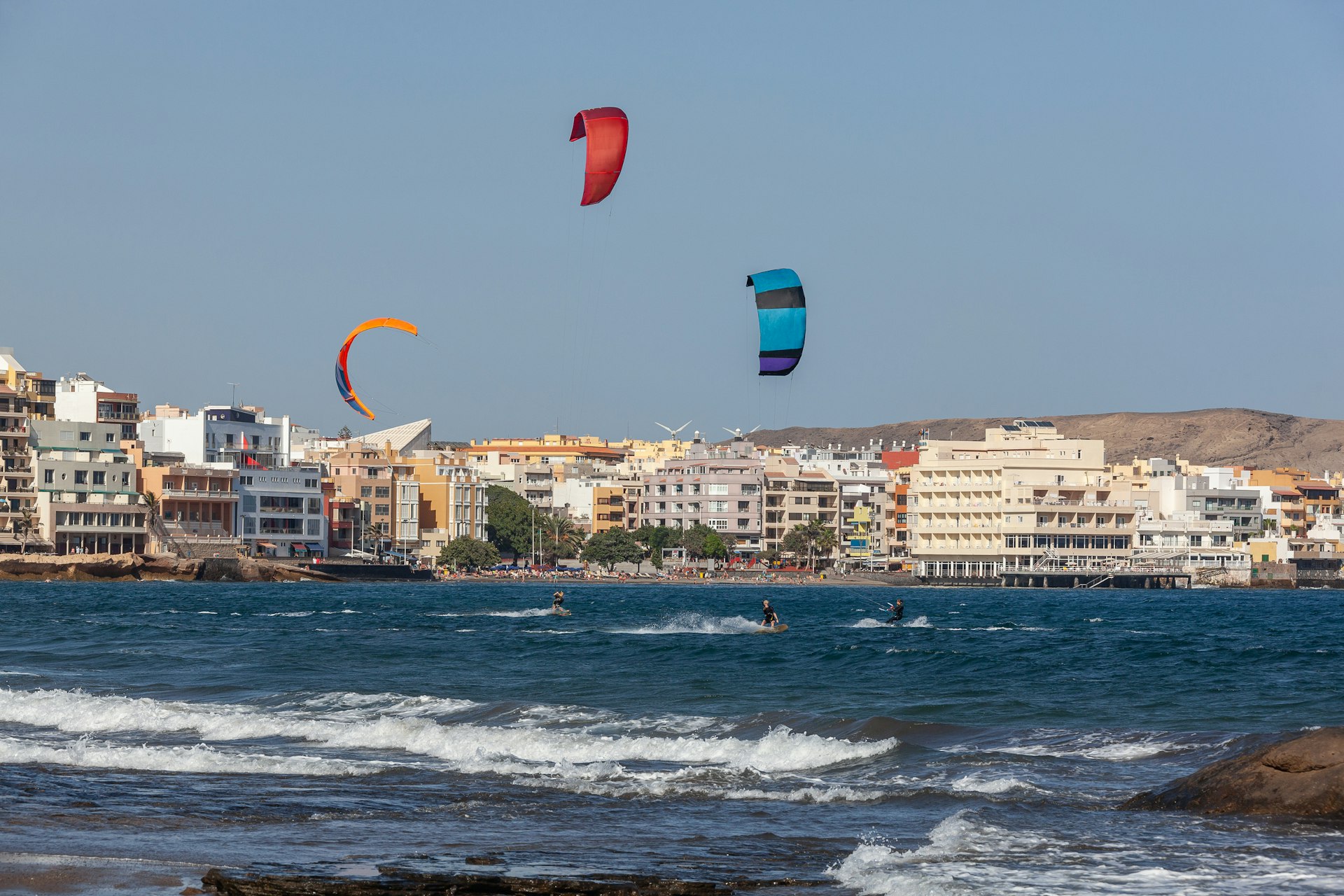 Three kitesurfing kites fly above surf at the beachside village of El Medano