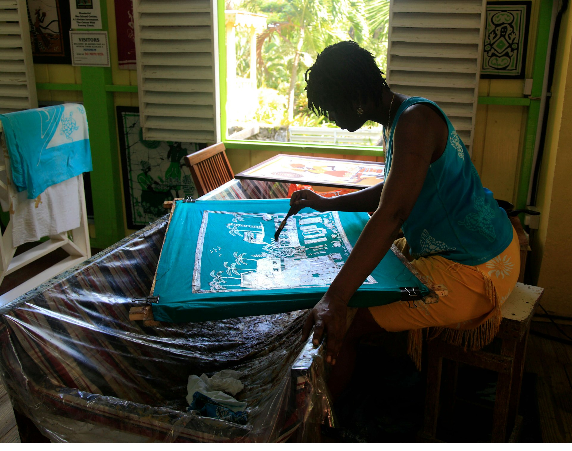 A woman paints on a piece of turquoise material stretched over a frame