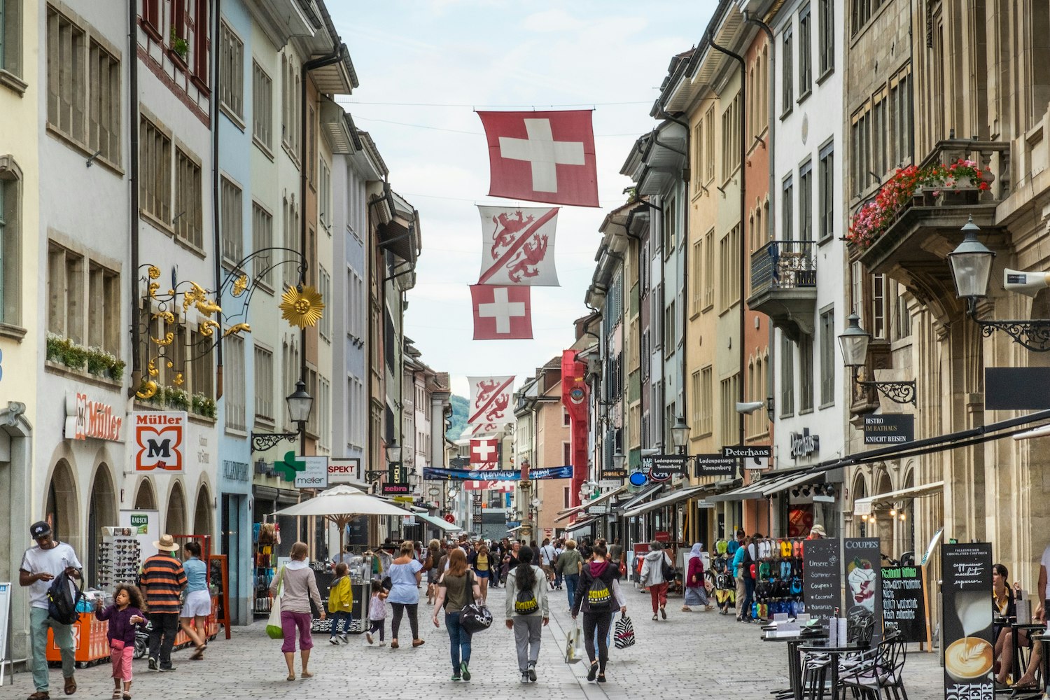 Under Swiss flags, pedestrians walk down busy Marktgasse toward the city center of Winterthur, Switzerland