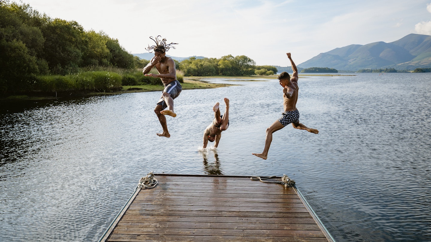 Young multi ethnic guys jumping off a jetty into a lake in Derwent Water in Cumbria