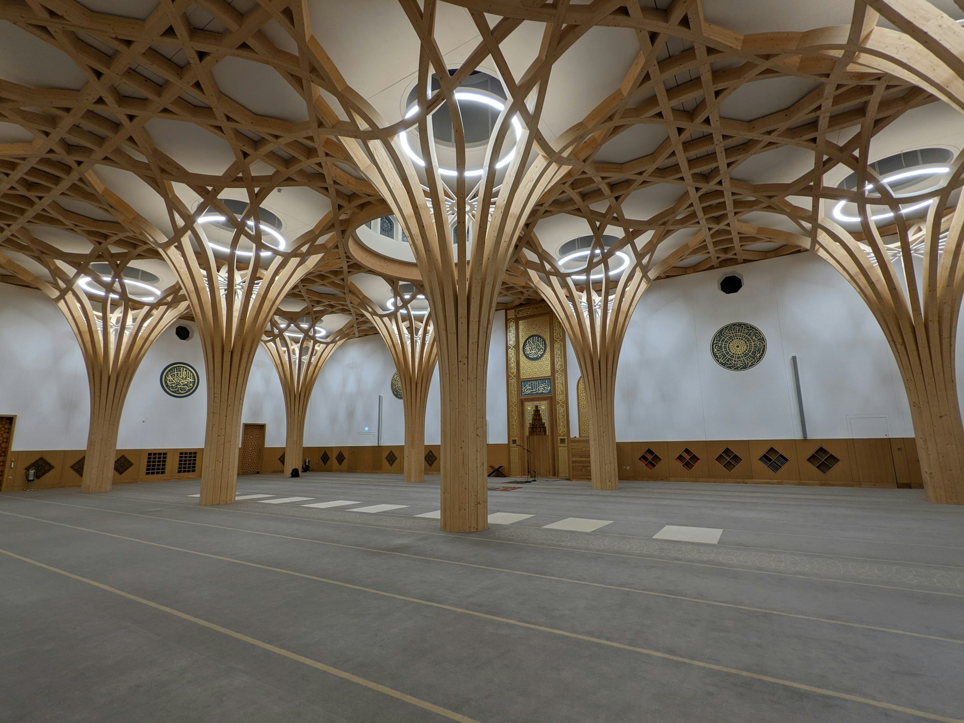 A large open space in a mosque with large arched wooden pillars leading to a light-filled space