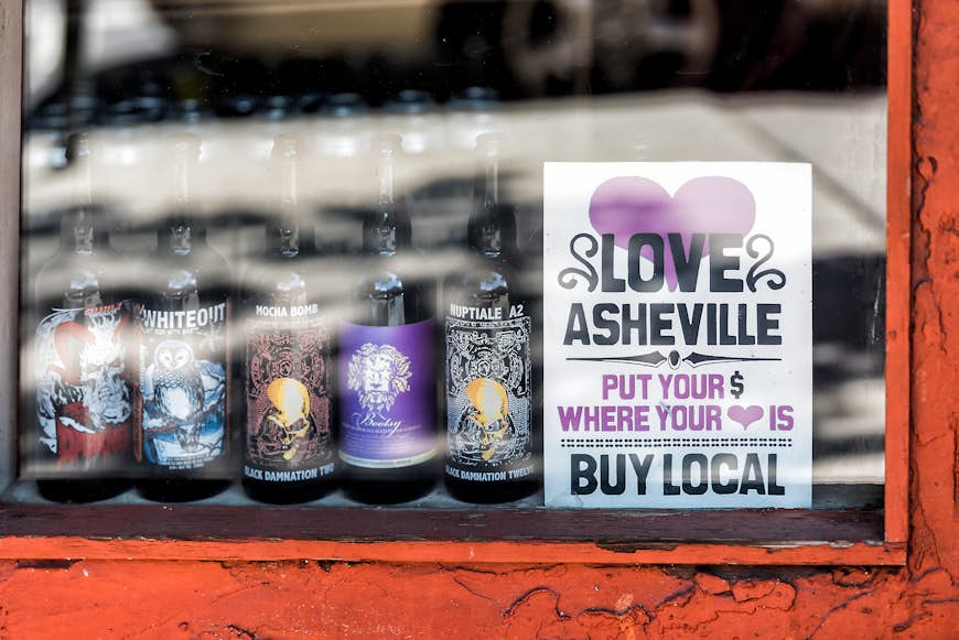 A window display of local beer bottles with a sign encouraging people to buy locally
