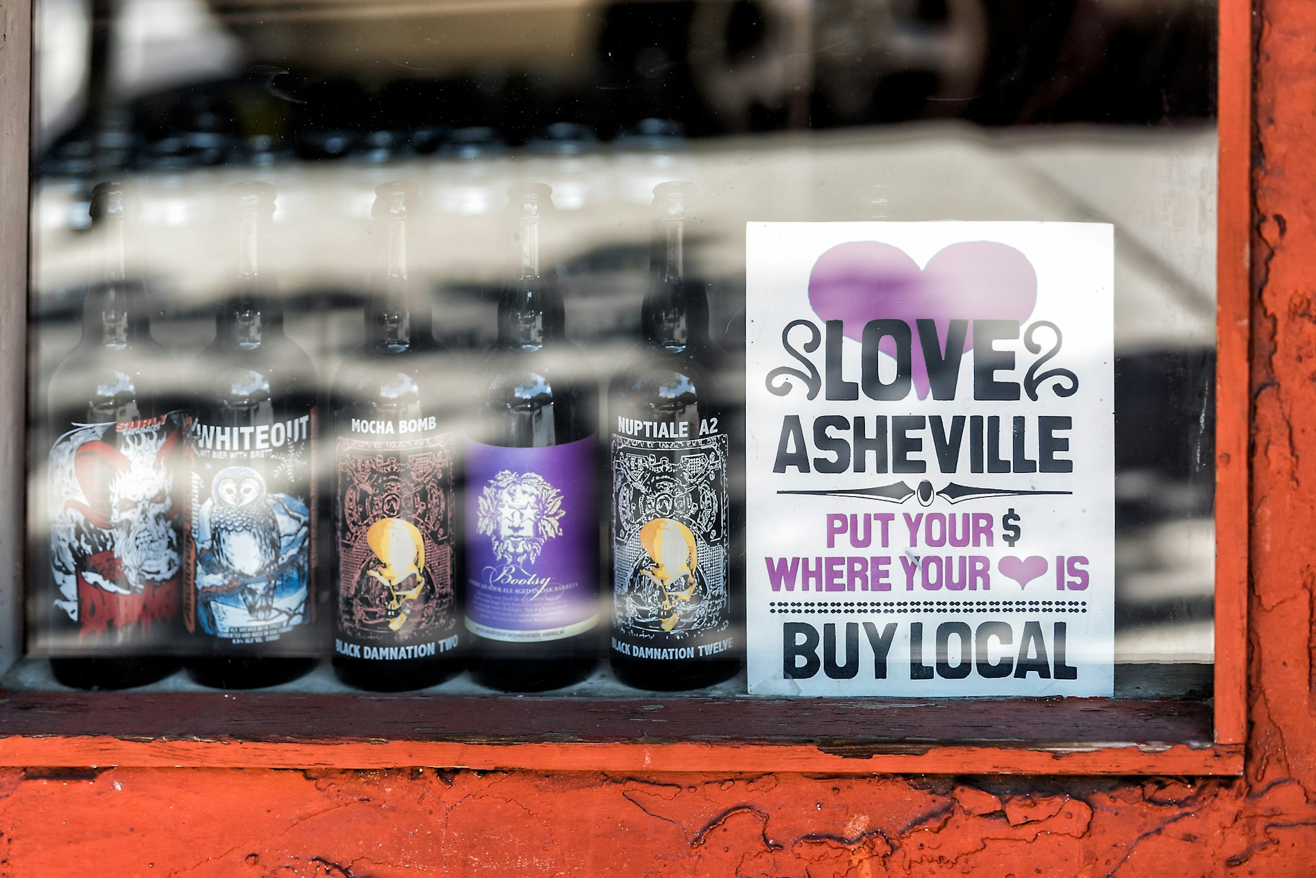 A window display of local beer bottles with a sign encouraging people to buy locally