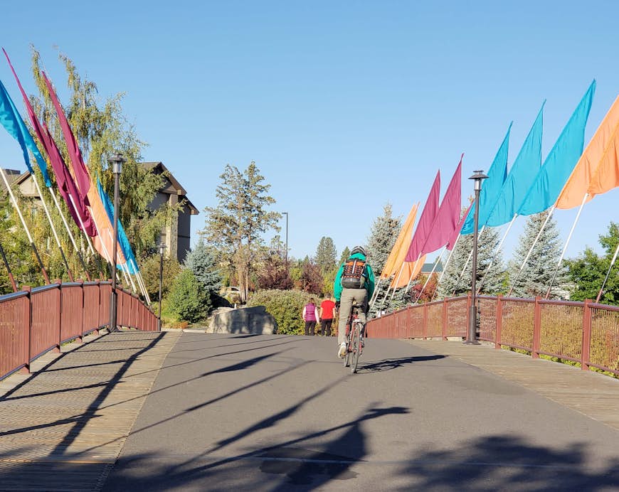 A bicyclist rides across a bridge with multi-colored flags that crosses the Deschutes River at the Old Mill District in Bend in Central Oregon