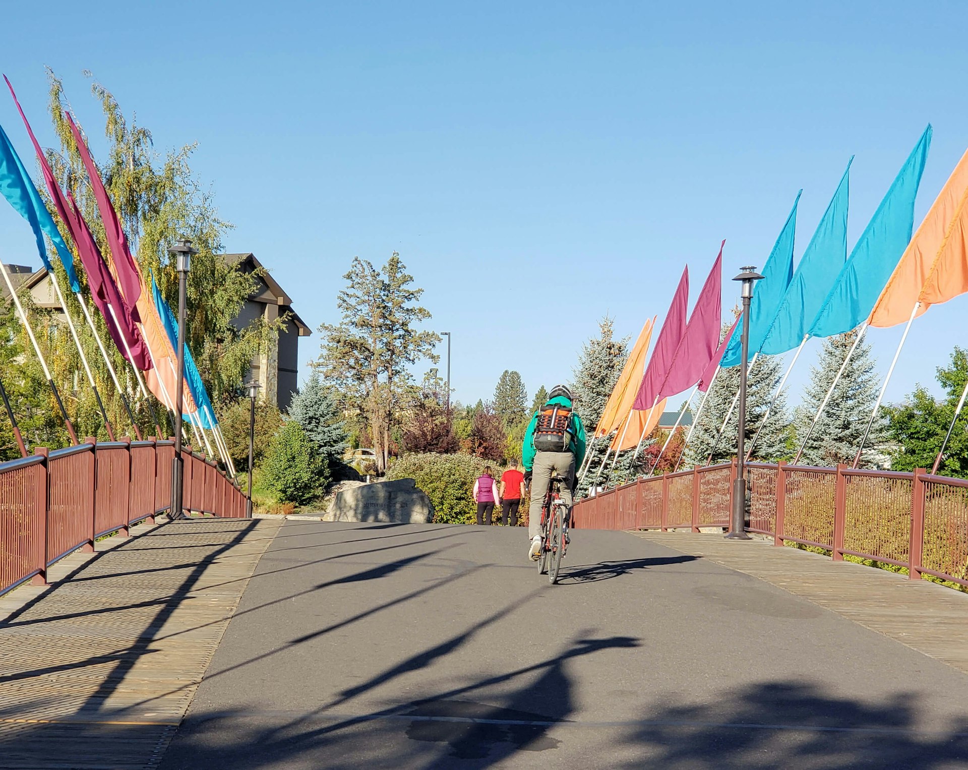 A bicyclist rides across a bridge with multi-colored flags that crosses the Deschutes River at the Old Mill District in Bend in Central Oregon