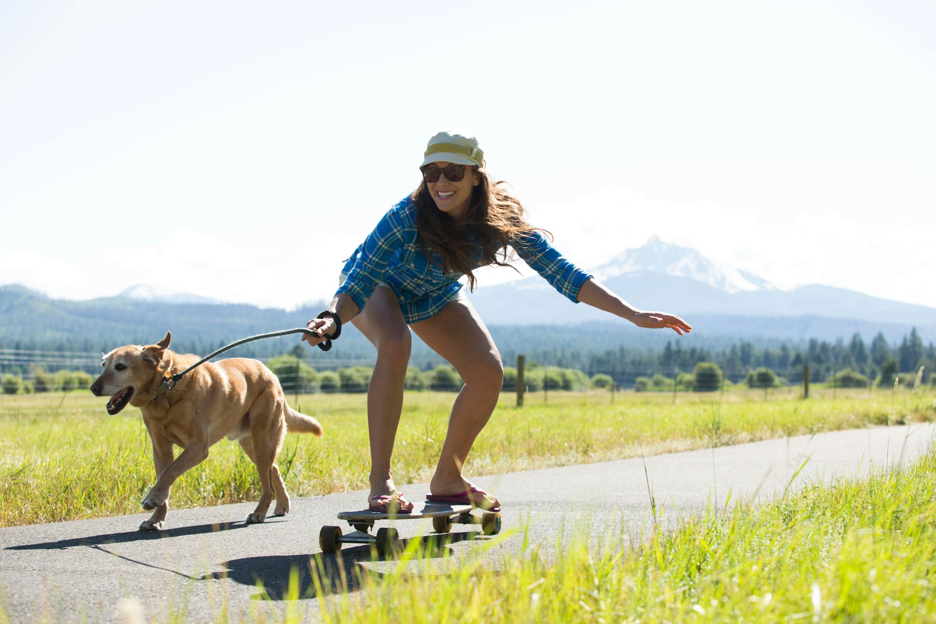 A woman skateboarding with her dog pulling her and a big mountain visible behind them