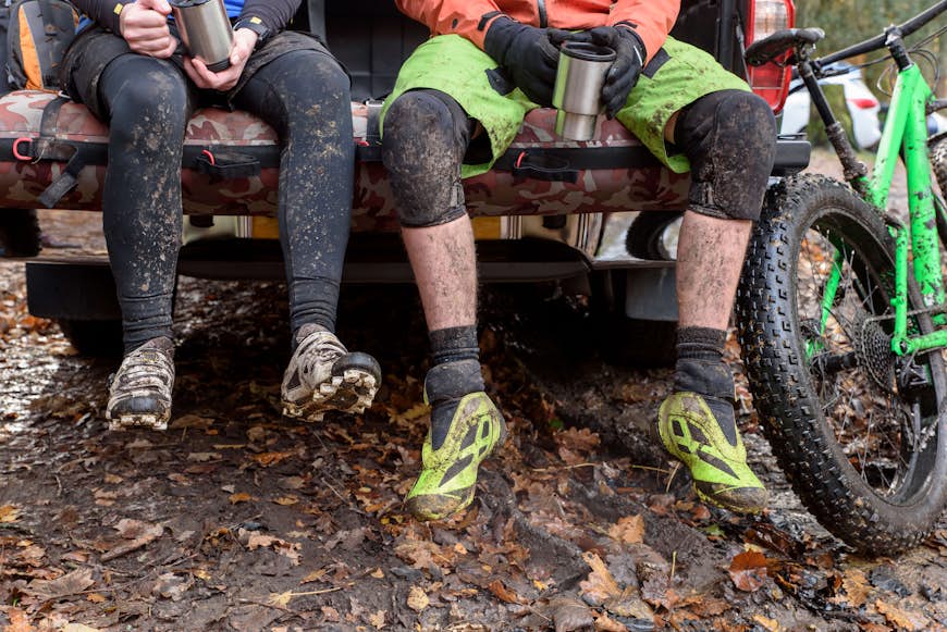 Muddy legs of Caucasian couple sitting in a pickup truck near a bicycle