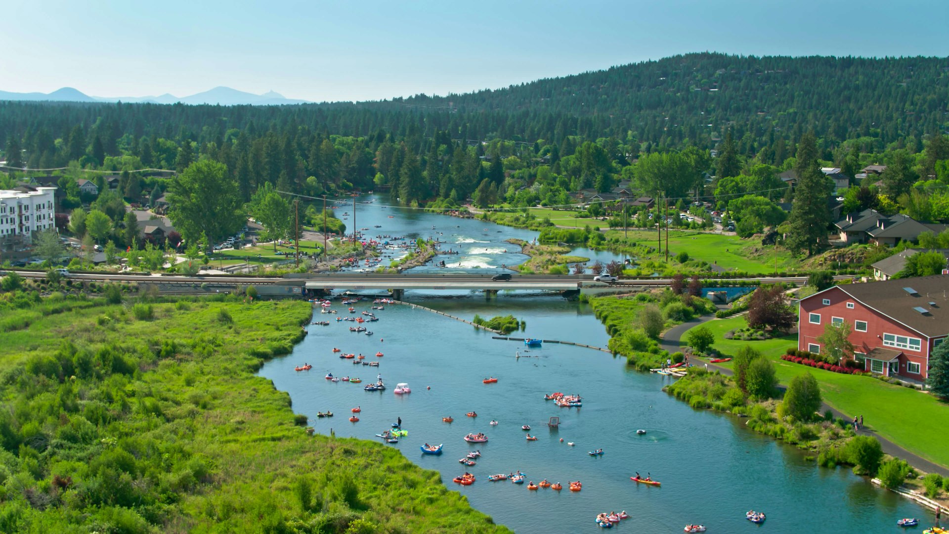 Aerial establishing shot of Bend, Oregon, on a hot and sunny day in summer. Scores of people are tubing, paddleboarding, kayaking and surfing in the Deschutes River