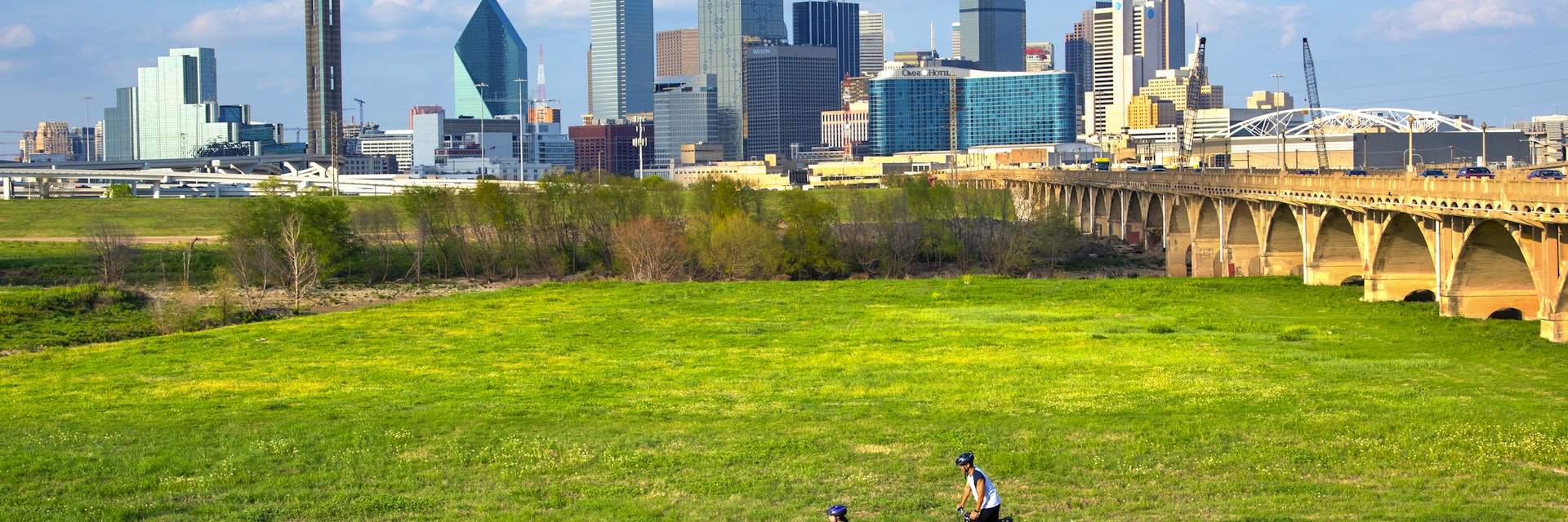 Cyclists on the bike trail in Trinity River Park with a backdrop of the Dallas skyline