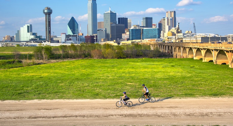 Cyclists on the bike trail in Trinity River Park with a backdrop of the Dallas skyline
