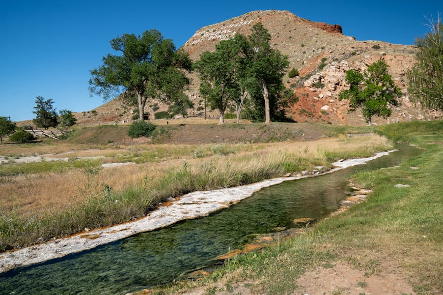 A small stream meanders through a meadow with a small mountain in the background - Hot Springs State Park in Thermopolis, Wyoming, a geothermal area in Hot Springs County