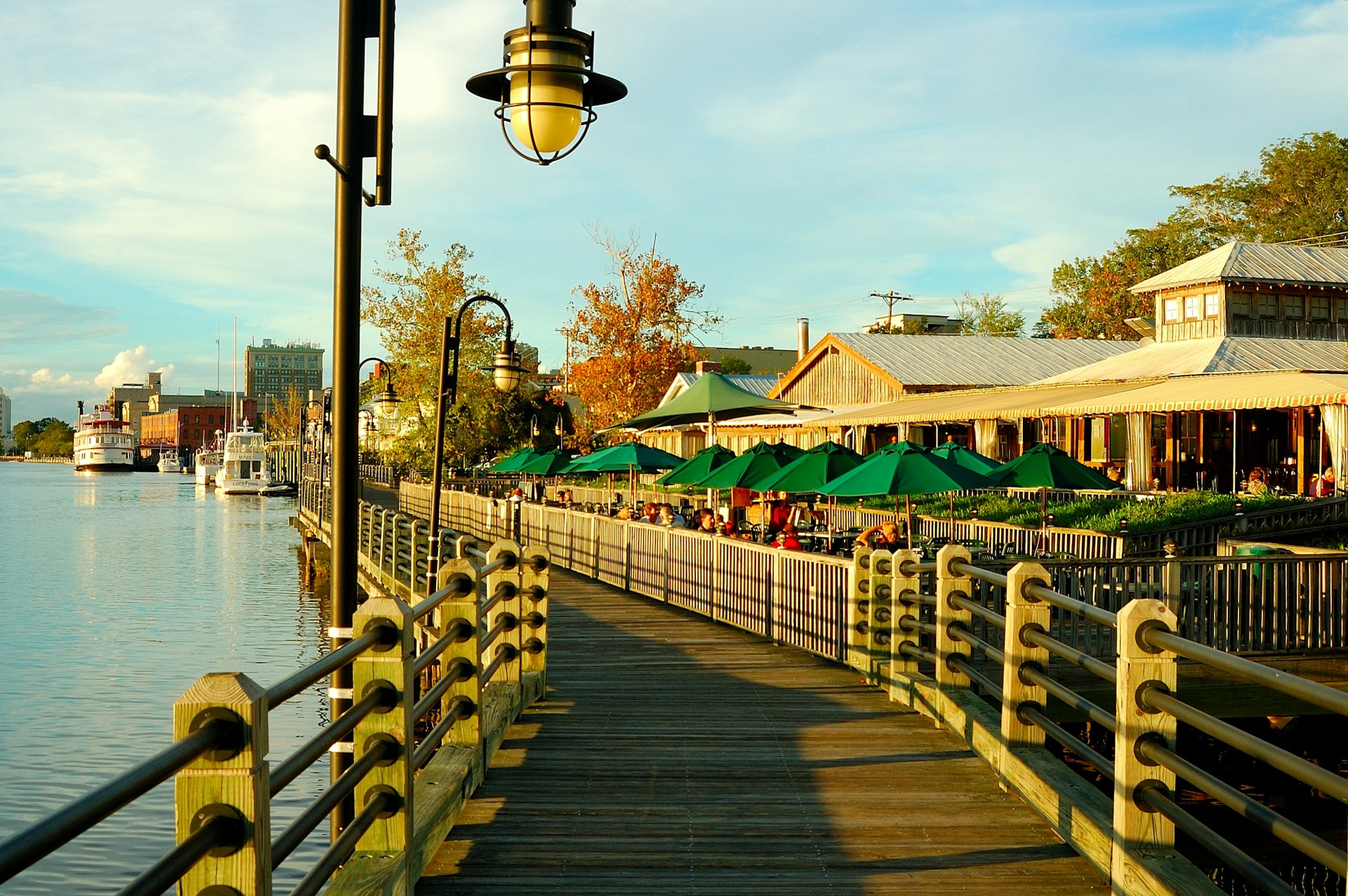 The Riverwalk in Wilmington NC at sunset with restaurants and boats lining the boardwalk on either side