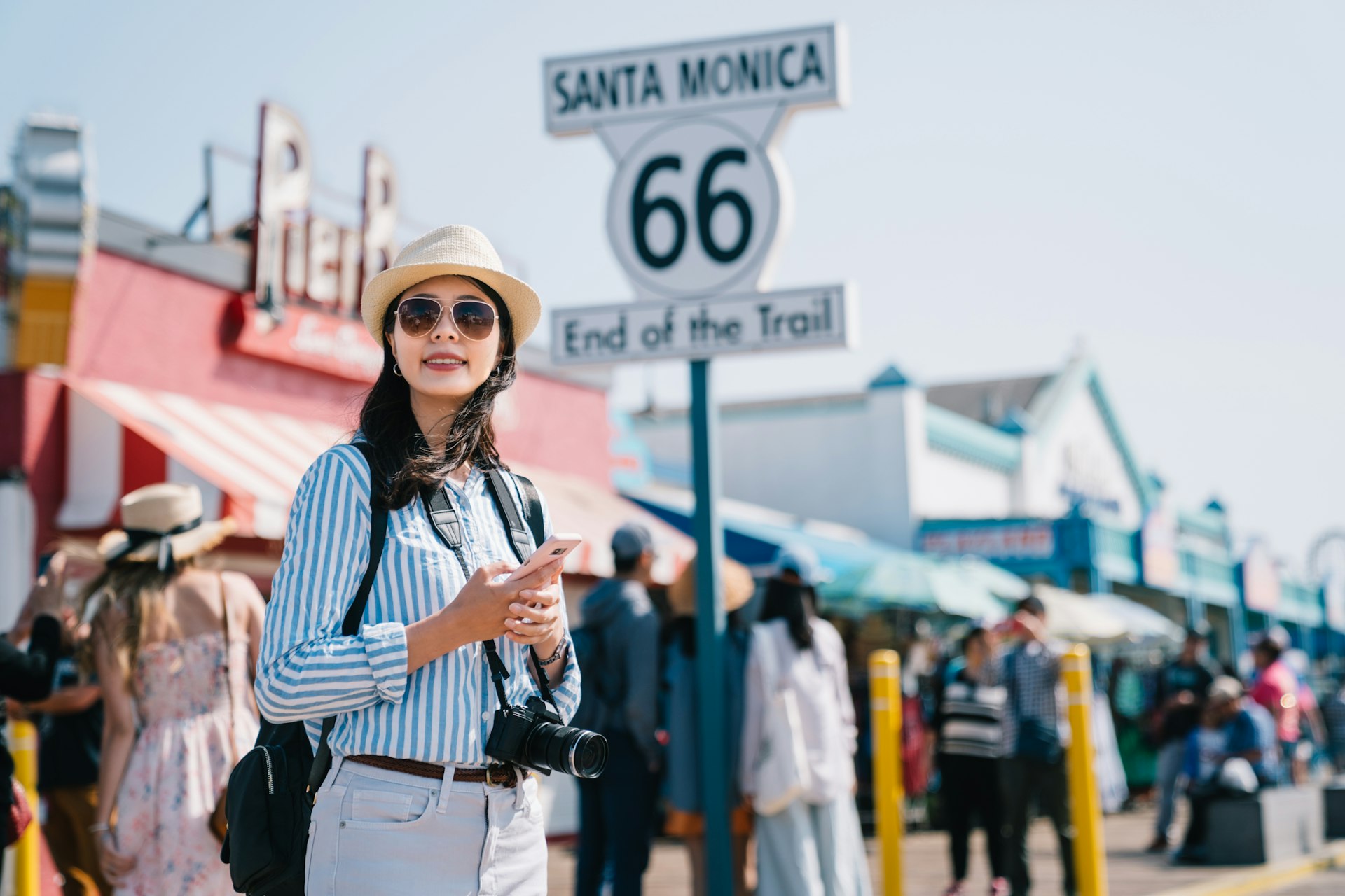A woman stands on the pier in Santa Monica near a large sign marking the end of Route 66