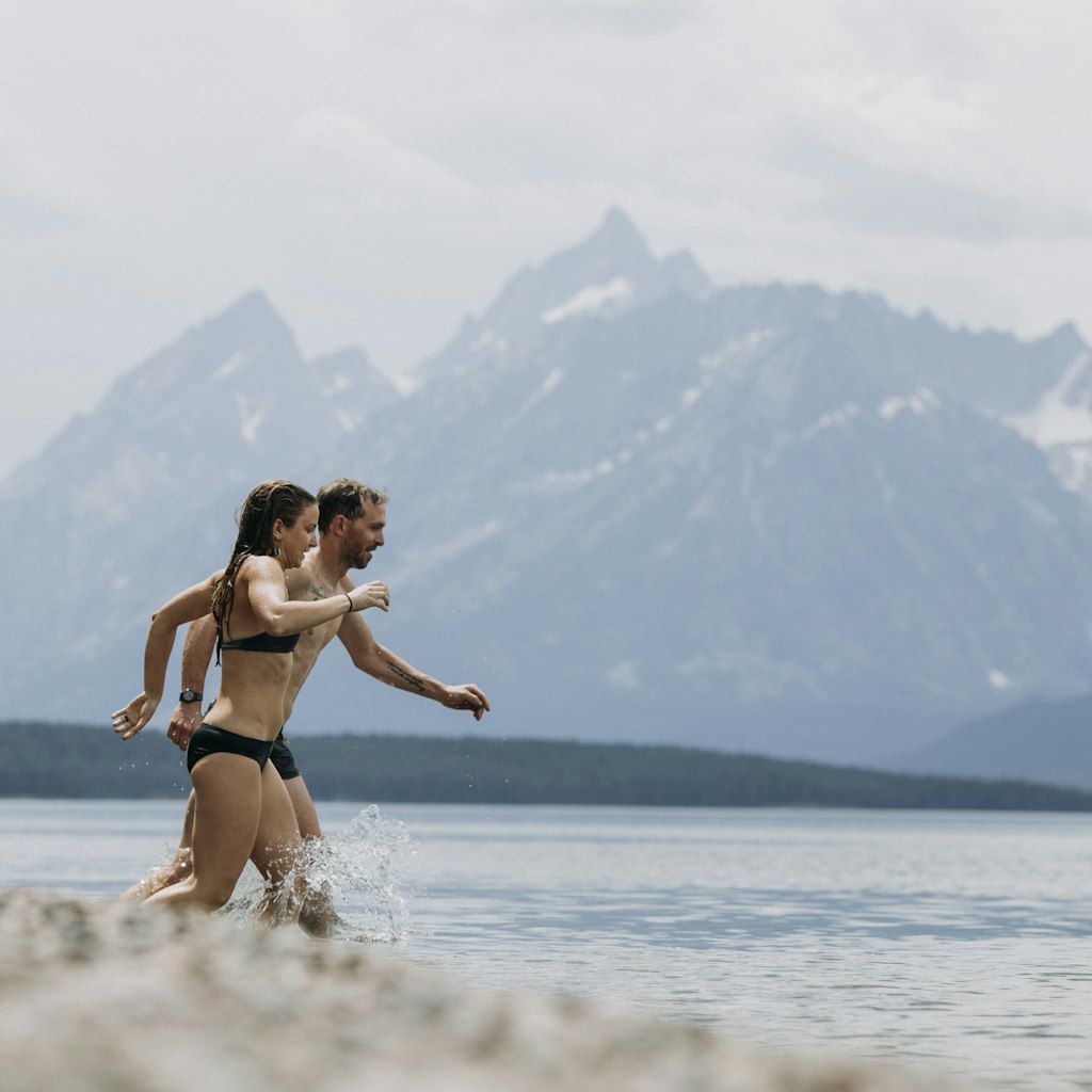 Couple runs into Jackson Lake for a swim, Tetons in the background