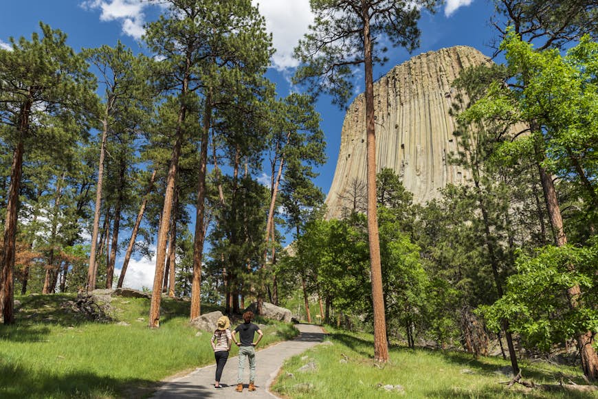 Двое туристов смотрят на высокое скальное образование, известное как Башня Дьявола, в Вайоминге, США.