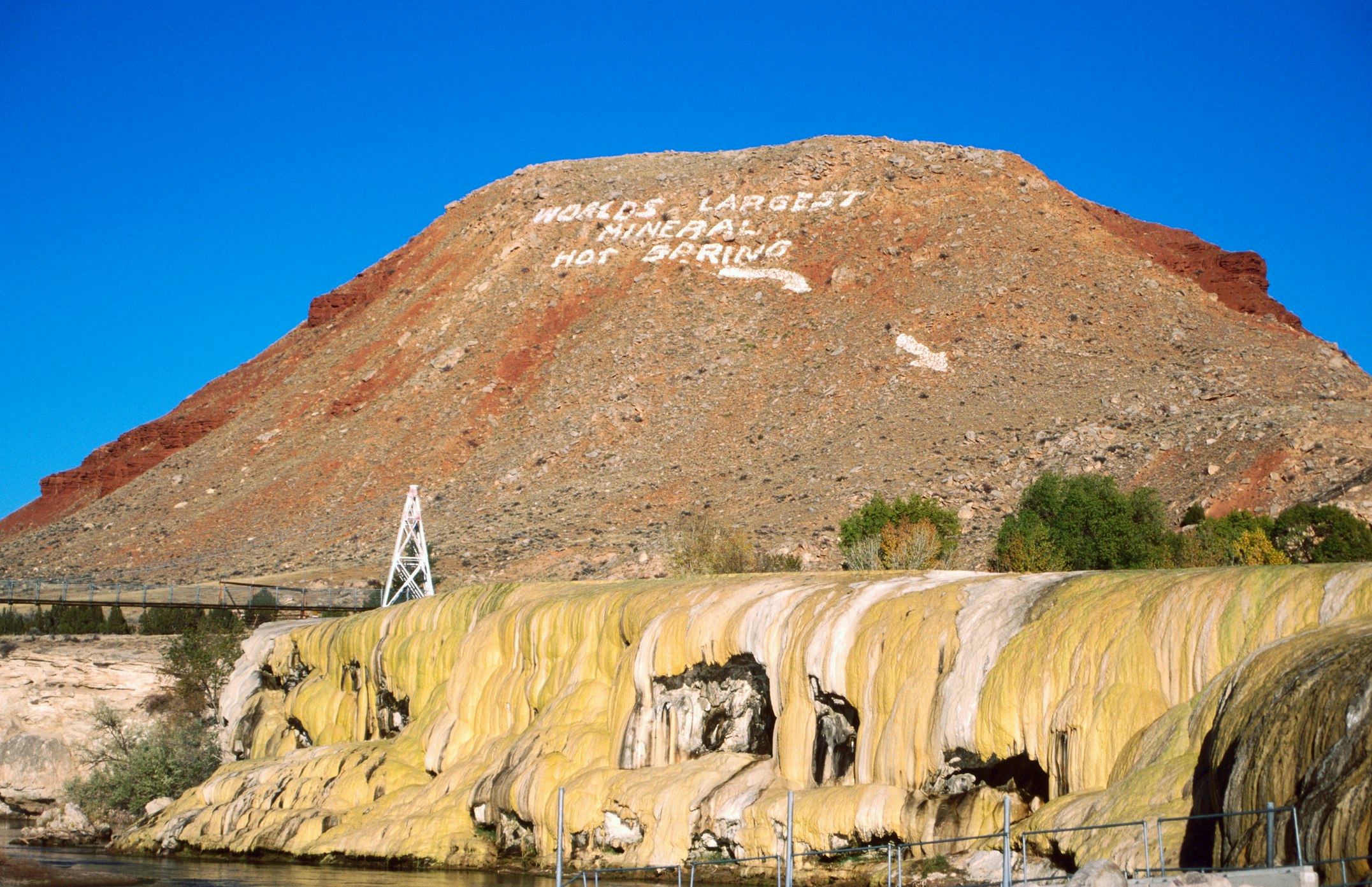 The words "World's largest mineral hot spring" are painted onto red rock above thermal pools at Hot Springs State Park in Wyoming