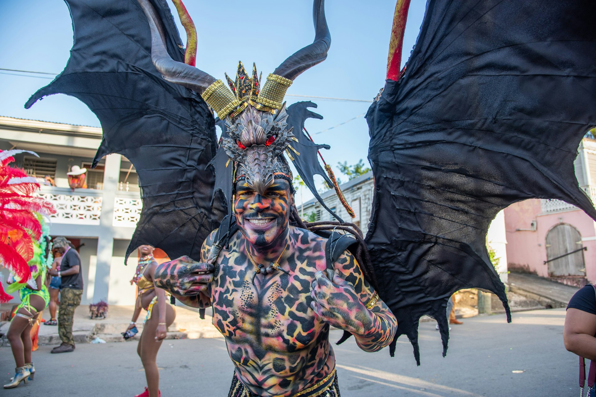 A man in a winged costume and covered in body paint smiles at the camera during Carnival in St Croix