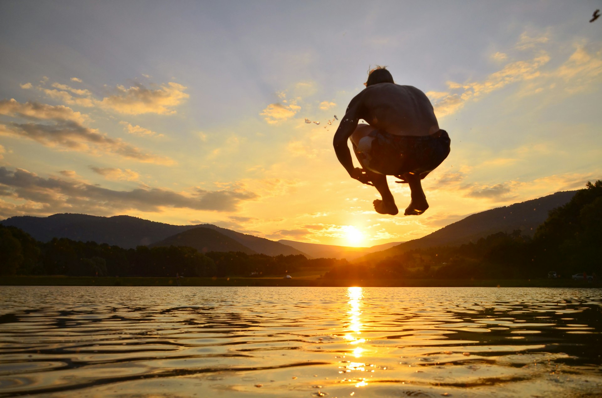 Young man jump onto summer water during calm sunset
