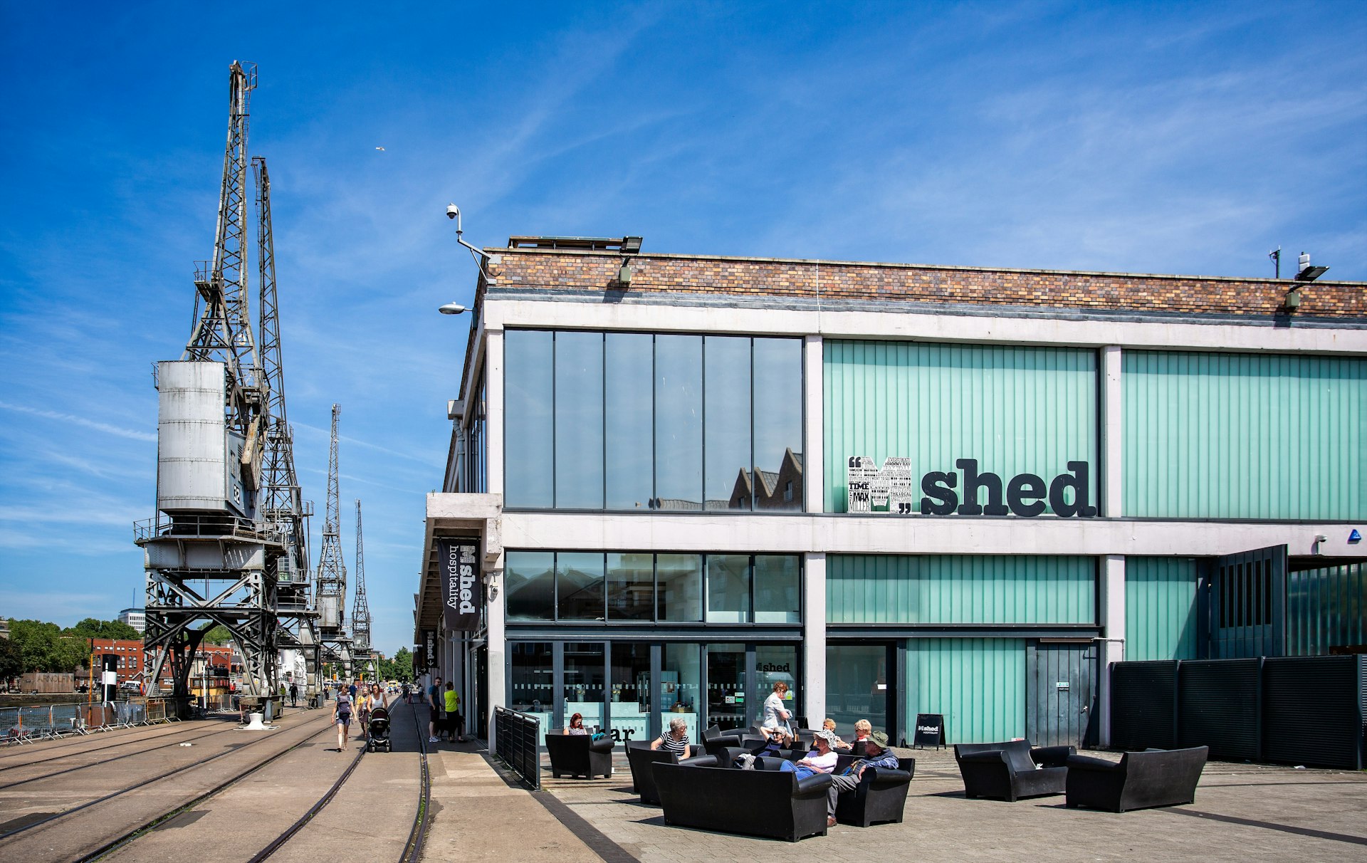 People sitting in front of the M Shed museum by gantry cranes in the former wharves of Bristol, Southwest, England, UK