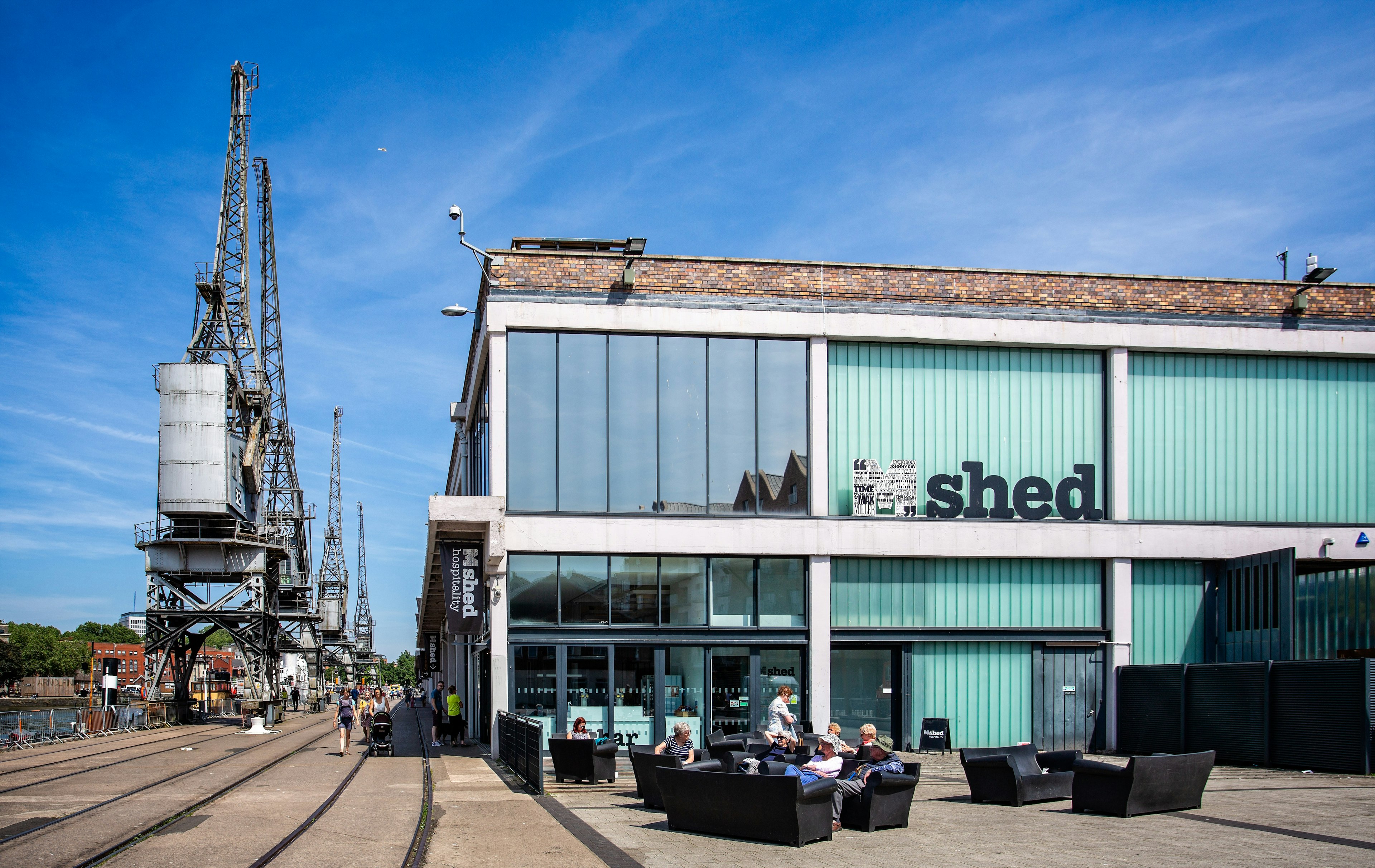 People sitting in front of the M Shed museum by gantry cranes in the former wharves of Bristol, Southwest, England, UK