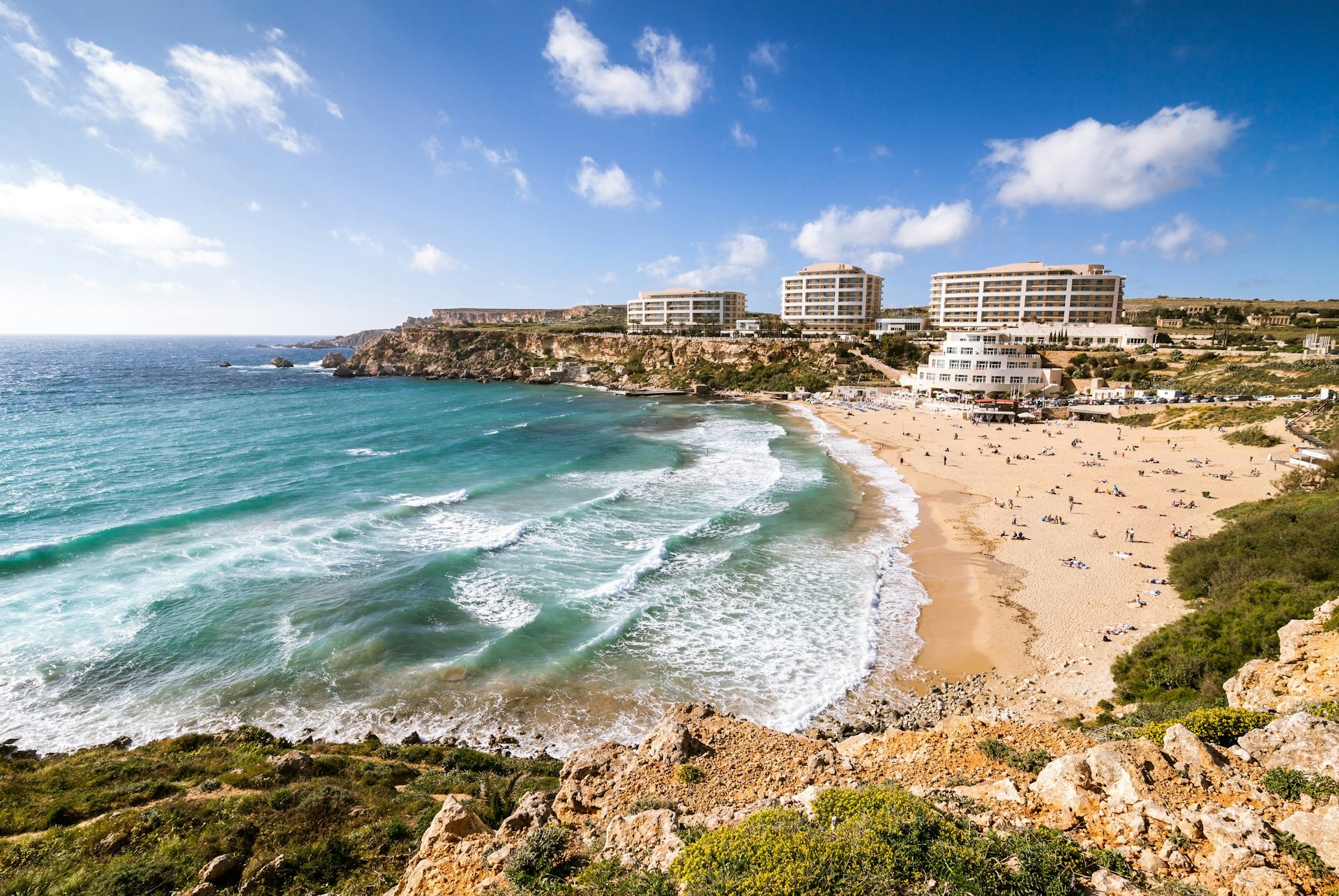Beachgoers gather in the sun at Golden Bay in Malta