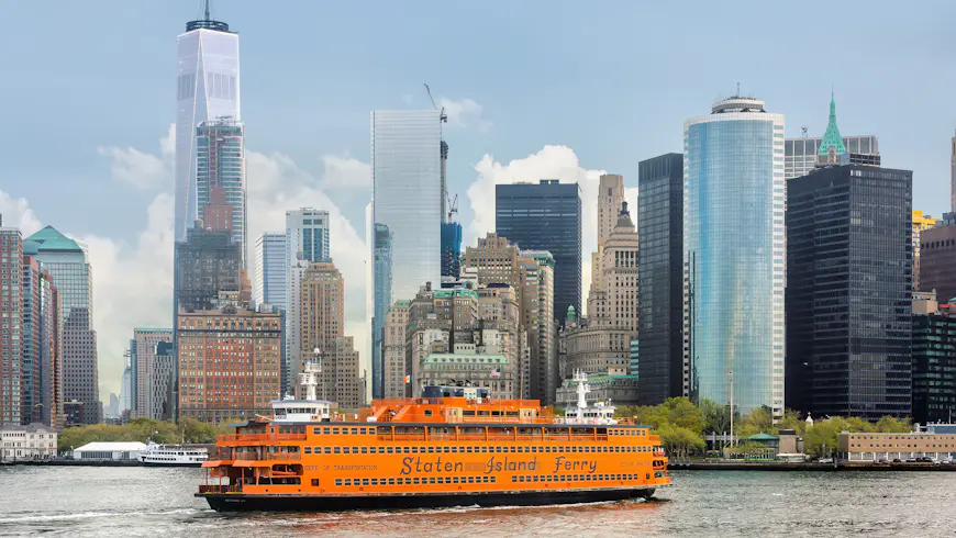 An orange boat of the Staten Island Ferry in New York Harbor against Lower Manhattan skyscrapers, New York City, New York, USA
