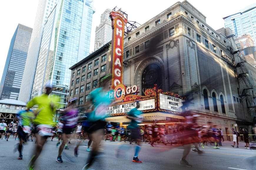 Chicago marathon participants run by the Chicago Theater with the red and white marquee lit up in the background. 