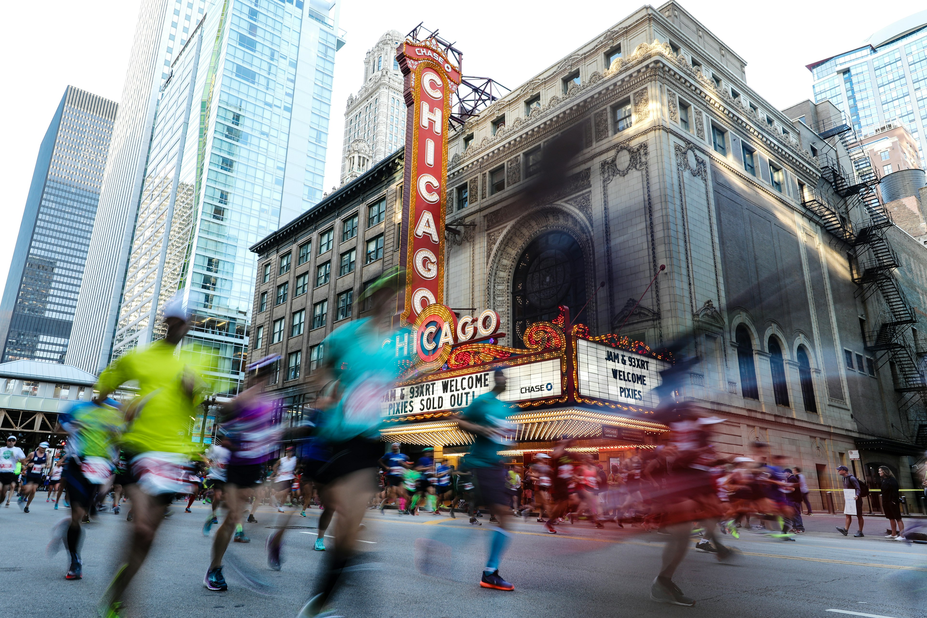 Chicago marathon participants run by the Chicago Theater with the red and white marquee lit up in the background.