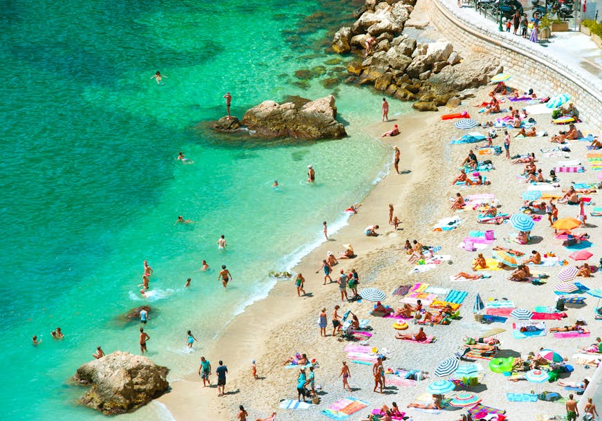 Аэрофотосъемка многолюдного пляжа и воды с множеством туристов и ярко окрашенными зонтиками от солнца в Вильфранш-сюр-Мер, Лазурный берег, Франция, Европа