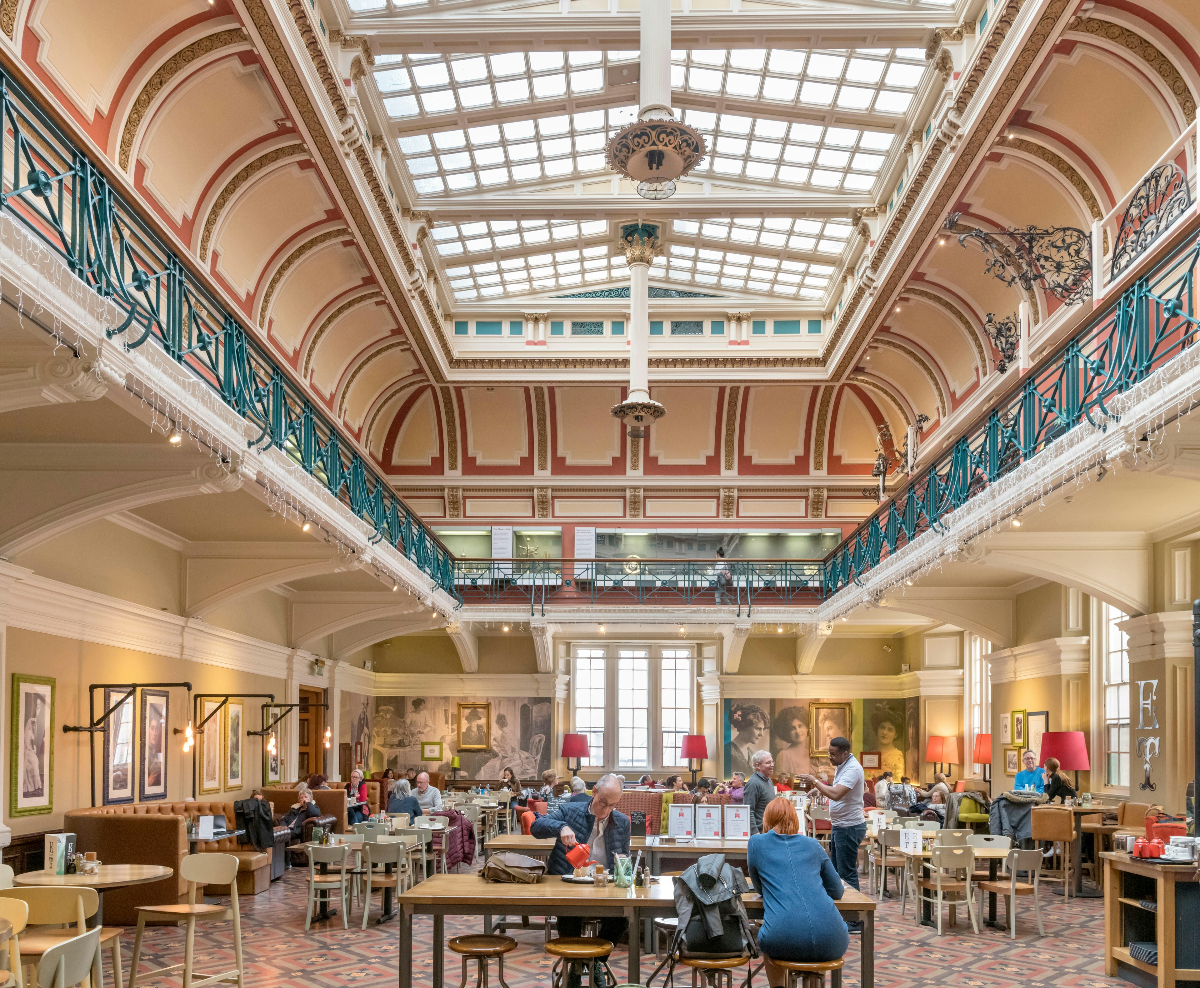 People in a large cafe with Edwardian decor around the walls and ceiling, and a mezzanine balcony